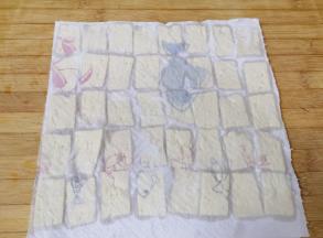 上面再盖上一层厨房用纸，吸去豆腐表面多余的水分，这样一会儿煎豆腐的时候就不会崩油了。