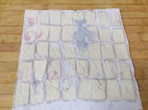 上面再盖上一层厨房用纸，吸去豆腐表面多余的水分，这样一会儿煎豆腐的时候就不会崩油了。