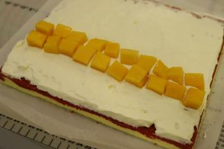 淡奶油加细砂糖打发至裱花状态，均匀地抹在蛋糕表面，1/3处摆放上切成小方块的芒果粒。