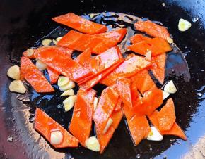 锅中倒入底油加热放入蒜爆香再放入胡萝卜片炒至断生