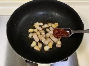 锅中倒入食用油，先入蒜片爆香，加入五花肉翻炒至变色，加入辣味黄豆酱。