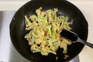 锅中倒入花菜翻炒至变软微焦，加生抽和蚝油翻炒。