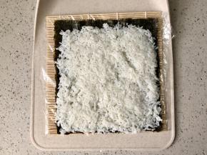 寿司席上可以先包一层保鲜膜，这样方便清洗。把海苔铺在寿司席上，先铺上一层米饭。米饭拌好寿司醋后要凉透后再铺到海苔上，否则太湿热海苔会起皱，而且不好切。