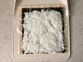 寿司席上可以先包一层保鲜膜，这样方便清洗。把海苔铺在寿司席上，先铺上一层米饭。米饭拌好寿司醋后要凉透后再铺到海苔上，否则太湿热海苔会起皱，而且不好切。