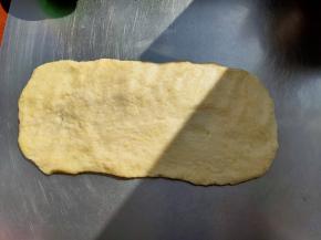 休息好的面团会比较柔软，延展性也很好，把面团转移到面板上，把面团整形成长方形的面片。