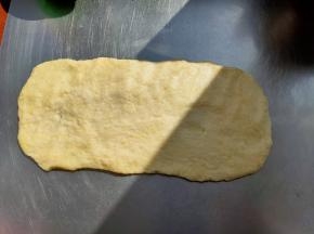 休息好的面团会比较柔软，延展性也很好，把面团转移到面板上，把面团整形成长方形的面片。
