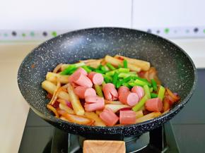 待年糕条均匀裹上酱汁时加入蒜薹及香肠。