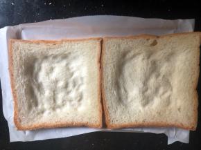 烤盘里铺油纸，摆两个吐司片。吐司片中间用勺子压坑，如图所示。