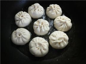 沿着锅边倒入半碗温水，大概包子的三分之一高度，然后盖上开始焖。水煮干后再倒一次水，再焖一次。注意，水不要直接倒在包子上。水煎时火最好再调小一点，就是煤气灶外圈火将熄未熄时。
