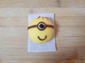 将可可面团擀成薄薄的片，用剪刀剪出小黄人的装饰部分，黑色面团搓出小黄人眼睛的眼珠，各部件沾水将小黄人组装好。