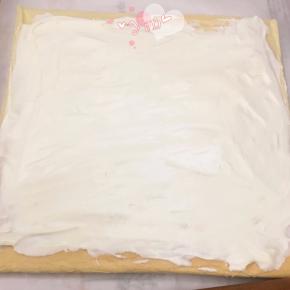 晾凉翻面，揭去油布，抹上淡奶油，放上橙子肉。用擀面杖卷住油纸，顺势往上推，卷起来，两边跟拧糖一样拧起来。放入冰箱冷藏半小时后再切块食用。