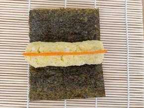 取70克的黄色米饭，捏成圆柱，放在2/3的那块海苔上，把胡萝卜条也放上