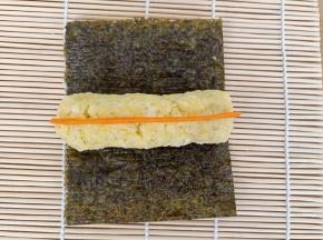取70克的黄色米饭，捏成圆柱，放在2/3的那块海苔上，把胡萝卜条也放上