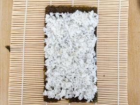 将最后一块海苔铺在卷帘上，1/3的那块也一起拼接起来，否则最后长度会不够，将90克的米饭均匀铺在上面