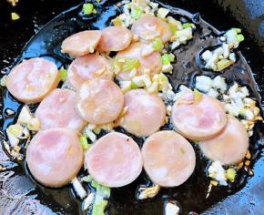 锅中倒入底油加热放入葱、蒜粒爆香再放入香肠翻炒片刻