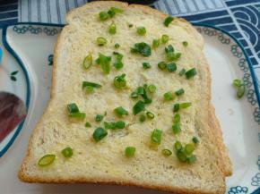 把涂完黄油的面包片表层撒一些葱花，轻轻按压一下。