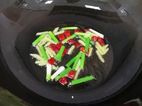 炒锅内倒适量的食用油烧热，下入葱白、姜丝和干红辣椒炒香。
