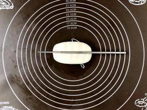 取一份面剂子，用手在案板上按扁，用筷子在按扁的面片中部稍用力压出小凹槽。