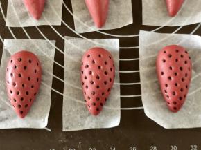 取一个粉色面团再揉光滑，用手心搓成一端大一端小的水滴状，尽量搓的细长一点，面团发酵蒸好后会变胖，形状就正好。用镊子夹芝麻粘在草莓上，镊子尖按压进面团。按压的深一点，否则蒸好后容易掉。