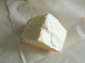 取一块戚风胚，尖角朝上，用锯齿刀从中切开一部分，千万不要切断。然后用抹刀将夹层里填满酸奶冰乳酪酱。然后在切面上也涂抹一层冰乳酪酱。