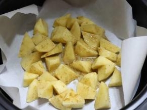 4.往空气炸锅里铺一层耐高温的油纸，然后摆上土豆块，垫油纸，主要是为了好清洁，这样烤都不用洗锅了，把油纸一扔就可以