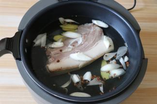将猪皮洗干净的猪肉整块放入锅中，加入适量冷水，放入大葱、一半的姜片、花椒、料酒；