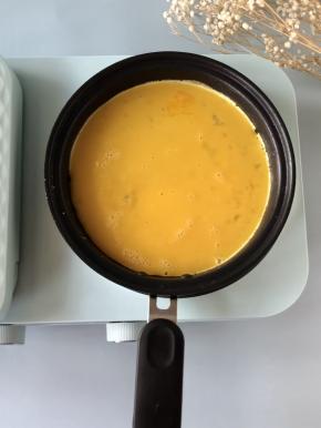油热后，火力调至低档，倒入一半的鸡蛋液，煎至底部凝固。