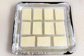 豆腐切成厚薄一致的块状，用刀尖在每块豆腐正反面浅划2～3刀，依次摆入垫有锡纸的烤盘中。