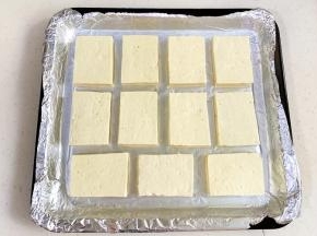 豆腐切成厚薄一致的块状，用刀尖在每块豆腐正反面浅划2～3刀，依次摆入垫有锡纸的烤盘中。