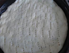 把发酵好的面团弄成圆形放入披萨盘中，保温保湿发酵约20反正，然后在表面用叉子扎孔