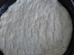 把发酵好的面团弄成圆形放入披萨盘中，保温保湿发酵约20反正，然后在表面用叉子扎孔