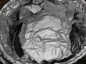 5.在三脚架上放入一块锡纸，四周像盘子边缘一样折起来，防止烤肉时烤出的水分滴落到砂锅里