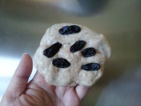 将一份面团轻轻压扁，包入几粒葡萄干。