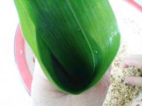 取两片粽叶，一片长一点宽一点的放下面，一片窄一点的放上面，然后从中间折成一个杯状。底下不能有洞，会漏米的。