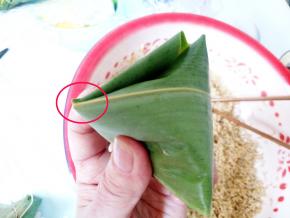 叶子盖下来后，在左手尖角那折过去，贴住粽子。