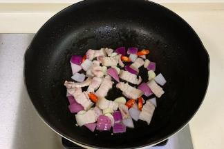 往锅中放入蒜片、小米辣和洋葱爆香，加入五花肉炒至变色。