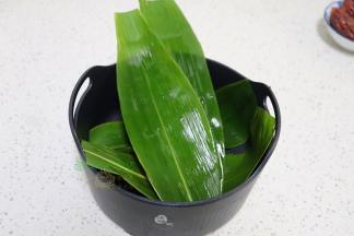 新鲜的粽叶清洗干净，用煮沸的水汆烫好，然后铺在电饭锅的蒸笼上。