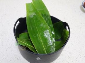 新鲜的粽叶清洗干净，用煮沸的水汆烫好，然后铺在电饭锅的蒸笼上。