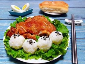 盘中铺上生菜摆上鸡腿肉米饭握成圆团撒上黑芝麻就大功告成了