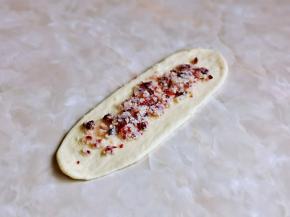 取一块面团，用擀面杖擀长舌状，再放上适当的蔓越莓椰蓉馅料，将两边对折再卷起来，收口擀薄捏紧。（收口一定要捏紧，避免发酵后爆开）