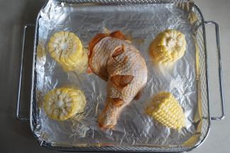 把腌制好的鸡腿放在烤篮上（烤篮铺上一张锡纸，防止油滴落在发热管上），玉米切成四段，用有盐黄油抹一下玉米，这样烤好的玉米更好吃