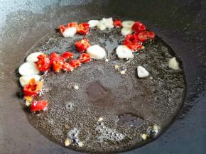 锅中热油，放入大蒜和干辣椒爆香。