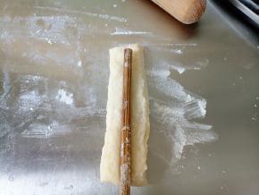 取一条面片，用筷子沾一点水，在上面轻轻压一下，然后将另一条面片盖上，再轻轻压一下，做成油条胚。