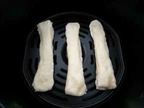 捏住油条胚两头轻轻拉抻一下，然后将刷油的那面朝下放入空气炸锅的炸篮中，表面也刷一层薄油。180度先烤5分钟。时间仅供参考，不同容量炸锅油条胚大小不同可能需要时间不一样，