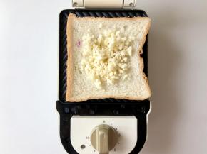 三明治机里放一片吐司，中间放上马苏里拉奶酪碎，用芝士片也可以。