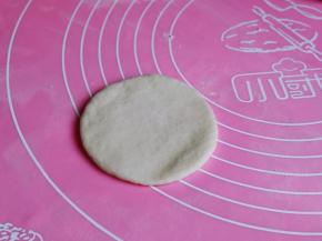 取一块白色面团，用擀面杖擀圆饼。