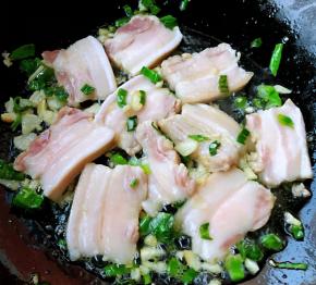 锅中倒入底油加热放入葱姜蒜爆香再放入五花肉炒至变色