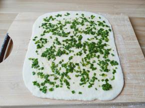 醒发好的面团排气，分成两个面团两次擀，取其中一个面团擀成厚一点的大长片，铺上葱花。