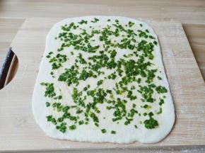 醒发好的面团排气，分成两个面团两次擀，取其中一个面团擀成厚一点的大长片，铺上葱花。