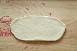 取一个松弛好的面团，拍扁，擀开成椭圆形，长度约为18CM。然后翻面。